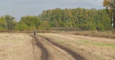 Kırsal alan, çiftlik. Yaşlı bir kadın biçilmiş buğday tarlasında eski bir bisiklete biniyor. Sibirya.