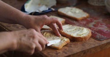 Yemek, ekmek. Ekmeğe tereyağı sürerek sandviç yapan yaşlı bir kadının elleri. Yakın plan..