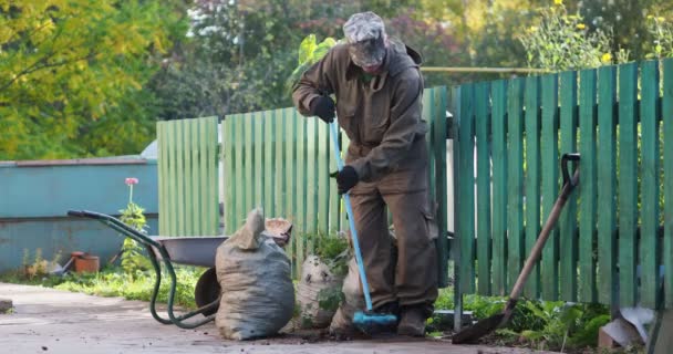 掃除だ 男が筆で歩道を掃くと 近くに埋められたゴミ袋があります シベリア — ストック動画