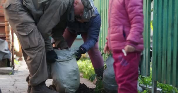 手仕事だ 家の近くの袋にゴミを入れている男と女のもとに小さな子供が走ってくる シベリア — ストック動画