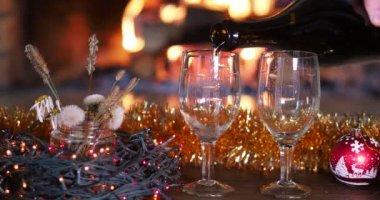 Tatil sezonu. Bir adam şömine ateşi ve Noel süslemelerinin arka planına karşı şişeden bardağa su dolduruyor..