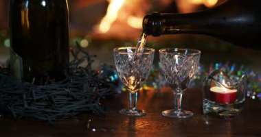 Tatil sezonu. Bir adam şömine ateşi ve Noel süslemelerinin arka planına karşı şişeden bardağa su dolduruyor..