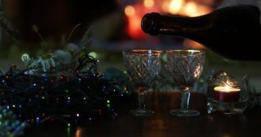 Tatil sezonu. Bir adam şömine ateşi ve Noel süslemelerinin arka planına karşı şişeden bardağa su dolduruyor..