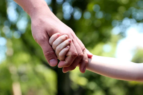 Un padre sostiene la mano de un niño pequeño sobre un fondo verde — Foto de Stock