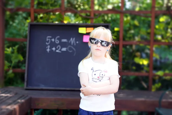 Nettes kleines Mädchen mit Pixelbrille vor der Tafel — Stockfoto