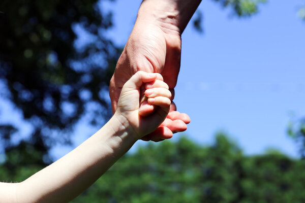 a father holds the hand of a small child on a green background