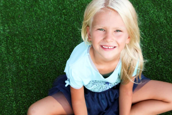 Schöne blonde lächelnde Mädchen sitzt auf dem Gras an einem Sommertag — Stockfoto