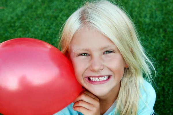 Mooi blonde lachende meisje zittend op het gras op een zomerdag — Stockfoto