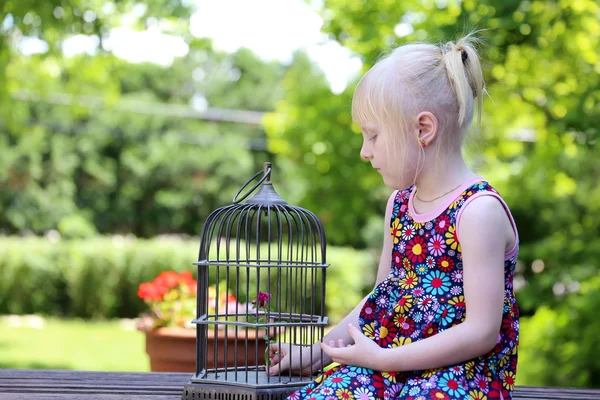 Schöne blonde Mädchen sitzt mit einem Käfig an einem Sommertag — Stockfoto