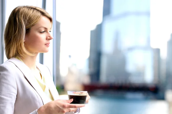 Portrait of business woman standing with coffee near window. Downtown area background — Stock Photo, Image