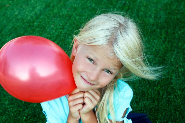 Belle fille blonde assise sur l'herbe et tenant une boule rouge — Photo