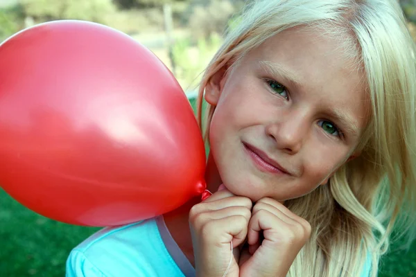 Belle fille blonde assise sur l'herbe et tenant une boule rouge — Photo