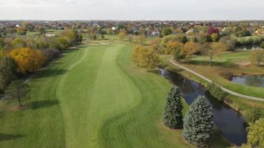 Göletli bir golf sahasının havadan görünüşü. Adam golf sahasında çim biçme makinesini hızlı kullanıyor. Golf sahasının yanındaki tek kişilik aile evleri.. 