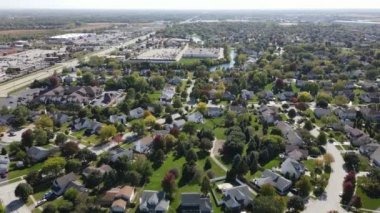 Chicago 'nun banliyö caddesi boyunca uzanan drenaj gölü olan renkli sonbahar ağaçlarının, konutların ve bahçelerin yukarıdan görünüşü. Amerika 'nın orta batısında. 4K
