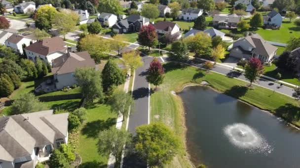 Overhead aerial view of colorful autumn trees, residential houses and yards with drainage pond along suburban street in Chicago area. Midwest USA. 4K — Stock Footage Overhead Aerial View Colorful Autumn Trees Residential Houses Yards Drainage Stock Video