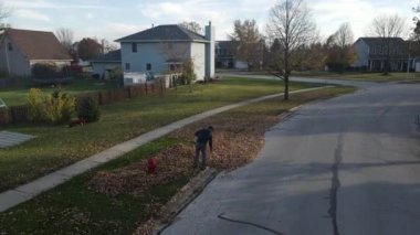 Bir banliyö caddesinde düşen sonbahar yapraklarını toplayan bir adamın hava manzarası. Amerikan banliyö mahallesi. Tek kişilik aile evleri. 4K