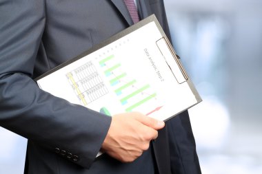 İşadamı ayakta ve elinde grafik tutarak .