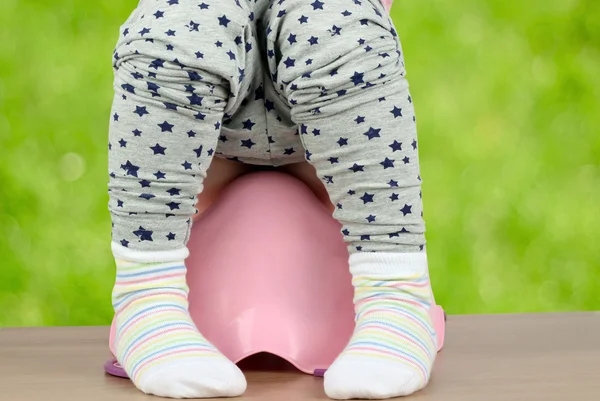 Kinderbeine hängen auf grünem Untergrund aus einem Topf herunter — Stockfoto