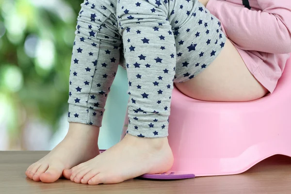 Barnens benen hänger ner från en kammare-pott på en grön backg — Stockfoto