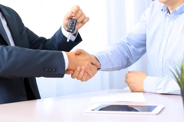 Car salesman handing over the keys for a new car to a young busi Stock Image