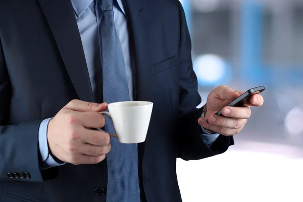 Bilden av en ung affärsmän stående på kontoret och hålla mobiltelefonen — Stockfoto