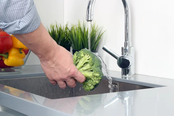 Homem lavando brócolis com água na cozinha — Fotografia de Stock