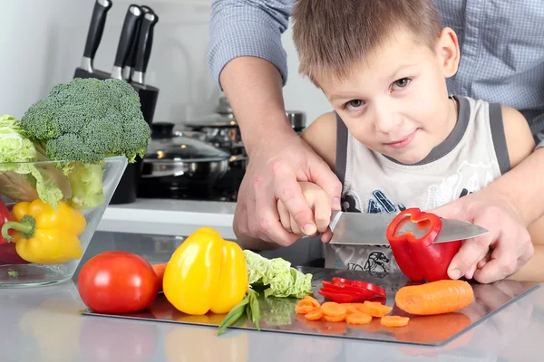 Comida, família, cozinhar e conceito de pessoas - Homem cortando páprica na tábua de corte com faca na cozinha com filho — Fotografia de Stock