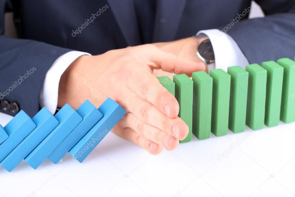 Close-up Of Businessman Stopping The Effect Of Domino With Hand At Desk
