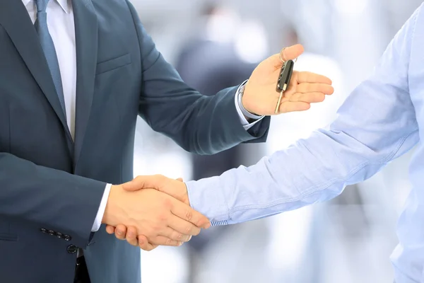 Car salesman handing over the keys for a new car to a young businessman . Handshake between two business people. Focus on a key