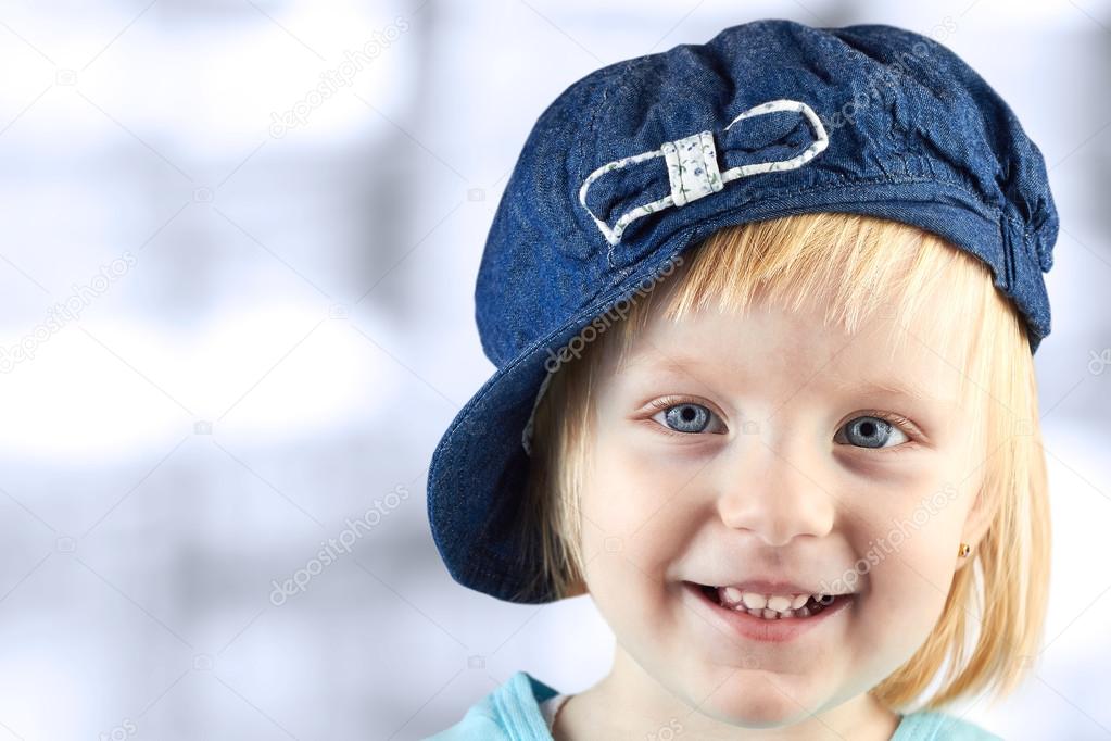 smiling  llittle girl   with a cap on her head on a blue  backgroun