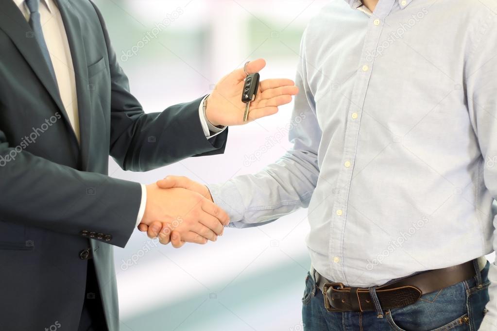 Car salesman handing over the keys for a new car to a young businessman . Handshake between two business people. Focus on a key