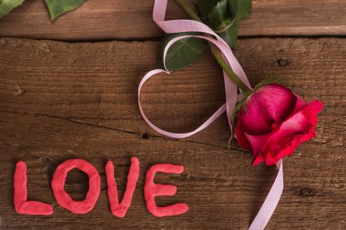 Etrafında kalp şeklinde pembe bir kurdele olan kırmızı bir gül çiçeği ve 