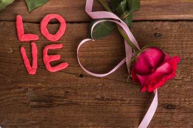 Etrafında kalp şeklinde pembe bir kurdele olan kırmızı bir gül çiçeği ve 