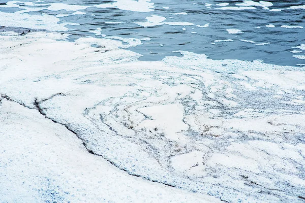 A burrowing river. The water drains through the concrete wall of the dam and flows into the river. Splashes and bubbles on the water. White foam on the water