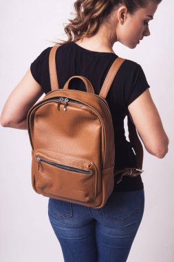 Güzel, genç bir kız stüdyoda kahverengi, deri bir sırt çantası gösteriyor. Deri aksesuar reklamı. El bagajı. Büyük, geniş el yapımı sırt çantası.