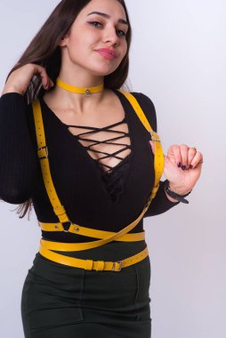 Avrupa görünümlü, güzel vücutlu genç bir kız kendi üzerinde deri bir aksesuar gösteriyor. Parlak deri giysi ayrıntıları. Kıyafetlerde şık kemerler. Deri