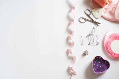 Dikiş malzemeleri - parlak renkli ipliklerle dolu bir kutu, pembe bir kurdele, pamuk, beyaz arka planda mezura. Çerçeve, metin için boşluk