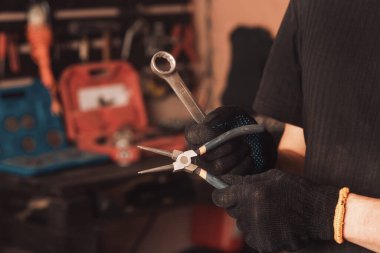 Tamirci elinde bir ingiliz anahtarı ve arabanın tamir aletleri olan bir panonun arka planında pasajlar tutuyor.