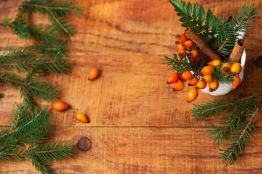 Kış, sıcak atmosfer. Ahşap bir arka planda ladin dalları ve gül kalçalari olan bir bardak kompozisyon. Yeni yıl geçmişi. Düz konum, metin yeri, kartpostal, çerçeve
