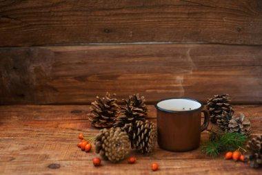 Kış, Noel arkaplanı kırsal tarzında. Metal, klasik kupa, gül kalçası böğürtlenleri, ladin dalları ve buğday dikenleri içeren kozalakların atmosferik bileşimi ahşap yüzeye yerleştirilir. Boşluğu kopyala, düzleştir