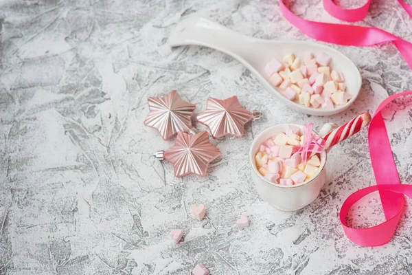 Silvester oder Weihnachten Komposition Tasse mit Marshmelow mit Süßigkeiten zwischen Neujahr, glänzendem Spielzeug und rosa Schleife — Stockfoto