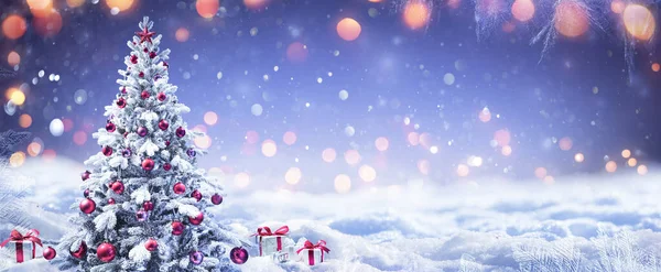 Kış manzarasında kırmızı süs ve hediye kutularıyla Karlı Noel Ağacı