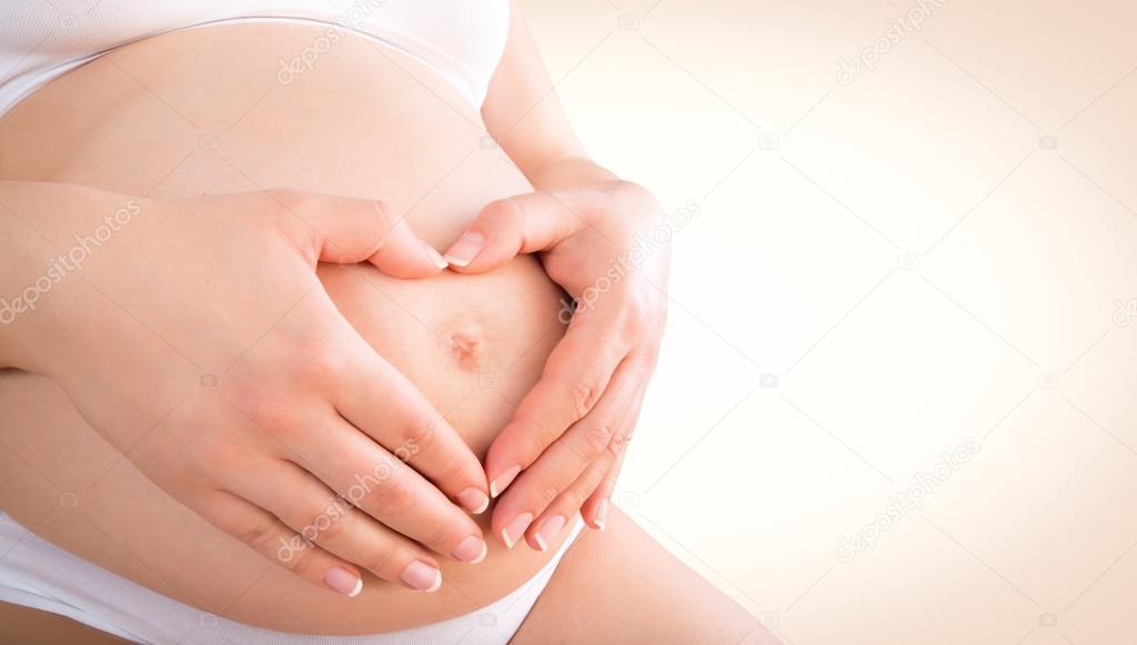 Pregnant woman embracing her baby bump with hands in a heart