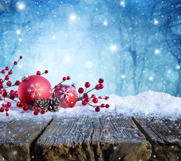 Roter Weihnachtsschmuck auf schneebedecktem Tisch mit Schneefall auf Hintergrund — Stockfoto