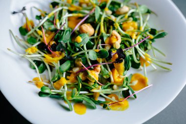 Koyu arkaplan, taze organik salata yaprakları ve beyaz tabakta daireler.