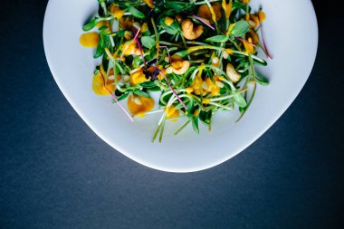 Koyu arkaplan, taze organik salata yaprakları ve beyaz tabakta daireler.