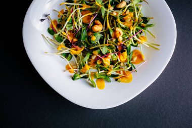 Koyu arkaplan, taze organik salata yaprakları ve beyaz tabakta daireler.