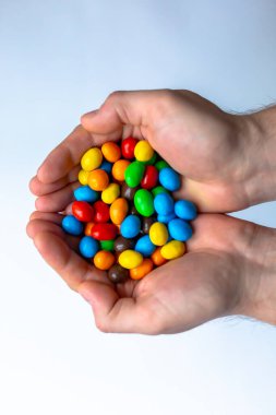 Beyaz arkaplanda renkli m & m şekerleri olan eller