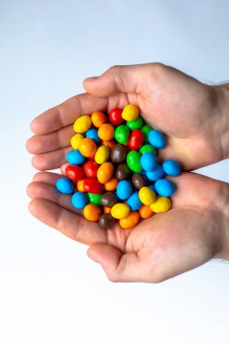 Beyaz arkaplanda renkli m & m şekerleri olan eller