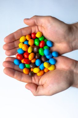 Beyaz arkaplanda renkli m & m şekerleri olan eller
